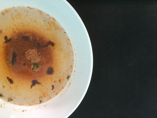 Soup with  seasoning sauce in white bowl placed on a black desk.