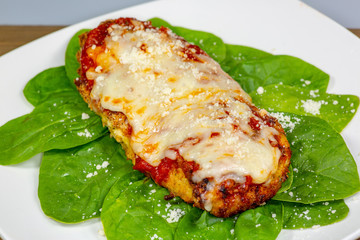 Chicken Parmesan on a bed of spinach with a sprinkle of fresh parmesan cheese on top on a white plate