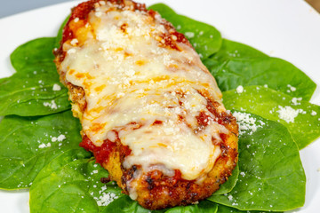Chicken Parmesan on a bed of spinach with a sprinkle of fresh parmesan cheese on top on a white plate