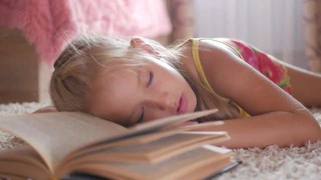Portrait sad schoolgirl does not want to study and read a book. A sweet blonde girl is sleeping on a book, she is tired when she did her homework.