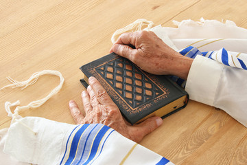 Old Jewish man hands holding a Prayer book, praying, next to tallit. Jewish traditional symbols....