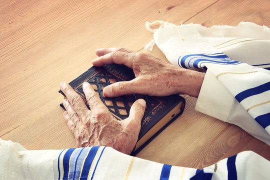 Old Jewish man hands holding a Prayer book, praying, next to tallit. Jewish traditional symbols. Rosh hashanah (jewish New Year holiday), Shabbat and Yom kippur concept.