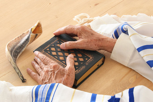 Old Jewish man hands holding a Prayer book, praying, next to tallit and shofar (horn). Jewish traditional symbols. Rosh hashanah (jewish New Year holiday) and Yom kippur concept.