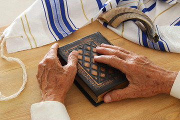 Old Jewish man hands holding a Prayer book, praying, next to tallit and shofar (horn). Jewish...