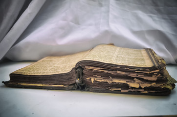 The old antique scruffy book "Bible" lies open on the table with white drapery. The concept of the teachings of Jesus.