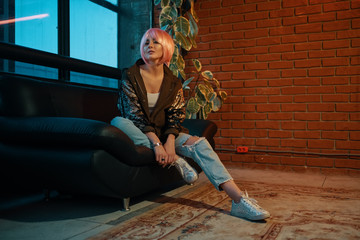 Girl with pink hair sitting relaxed on a leather sofa