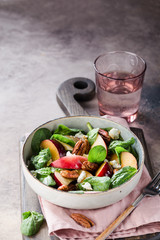 Bowl of salad with peaches, plums, spinach leaves, pecan nuts, honey and goat cheese on wooden cutting board. 