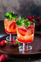 Red cocktail with ice, mint leaves and strawberry on wooden background.
