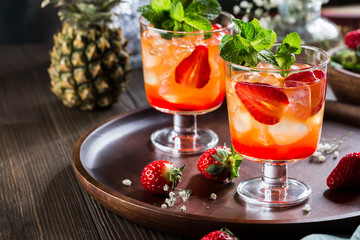 Red cocktail with ice, mint leaves and strawberry on wooden background.