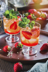 Red cocktail with ice, mint leaves and strawberry on wooden background.