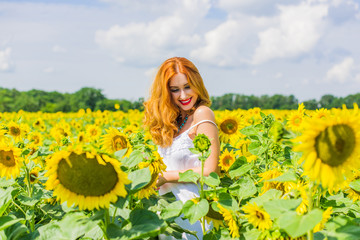 Fototapeta na wymiar Candid red haired woman in white dress in the sunflowers at middle of a field in summer. Wellness concept, positive emotions and lifestyle. 