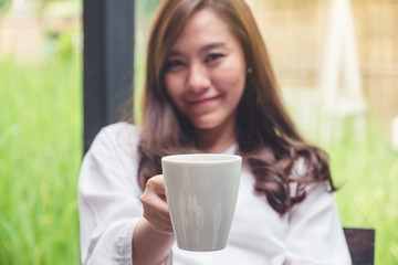 Closeup image of a beautiful asian woman holding and giving hot coffee with feeling good in cafe