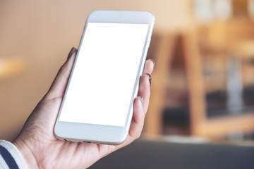 Mockup image of hand holding mobile phone with blank white screen in wooden cafe