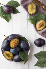 Fresh plum berries on a plate with leaves on a light table. Vertical. © Elenglush