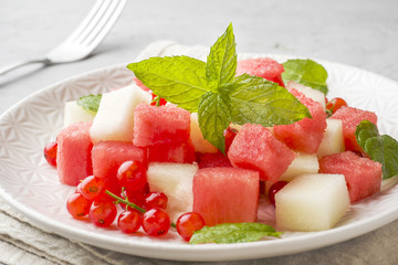 Salad of fresh juicy pieces of watermelon, melon, red currant and mint leaves on a plate.