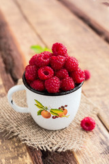 Red raspberries in a mug on wooden background. Rustic style.