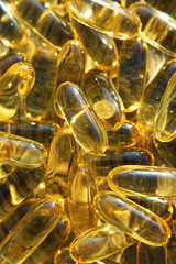 Pile of omega 3 fish liver oil capsules for heart health closeup view on grey weathered wooden surface outdoors with reflections from sunlight as textured background. Medicine, nutritional supplement 