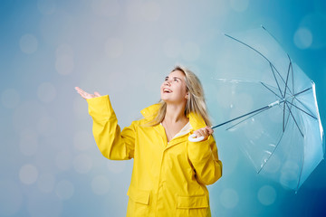 Blonde woman wearing yellow raincoat holding transparent umbrella checking weather if it is raining. Protected against rain and hurricane