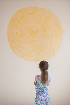 little pensive caucasian girl looking at yellow sun painted on wall indoors