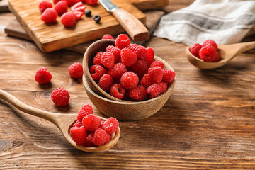 Bowl and spoon with fresh ripe raspberries on wooden table