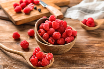 Bowl and spoon with fresh ripe raspberries on wooden table