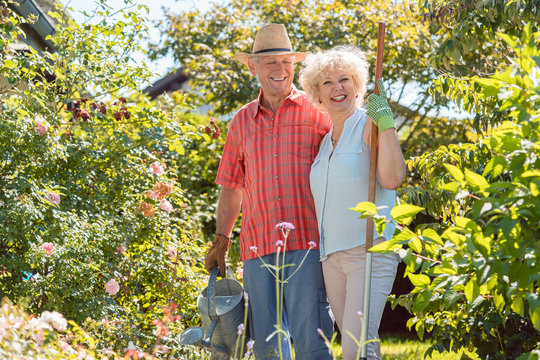 Active happy senior woman looking at camera while standing next to her husband during work in the garden in a sunny day of summer