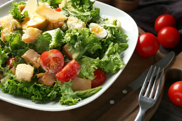 Plate with tasty Caesar salad on wooden board, closeup