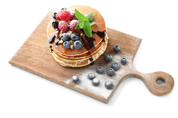 Tasty pancakes with chocolate sauce and berries on wooden board against white background