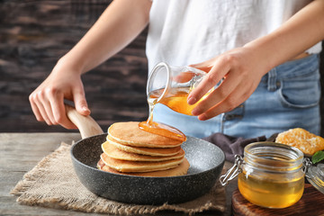 Woman pouring honey onto tasty pancakes at wooden table