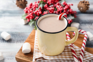Obraz na płótnie Canvas Metal mug of hot cocoa with candy canes on wooden board