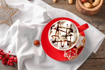 Cup of hot cocoa with marshmallows and cookies on table
