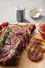 Tasty grilled meat with potato, sauce and herbs on parchment, closeup