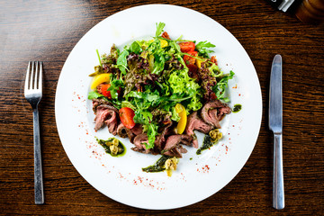 Appetizing meat dish served with tomatoes and lettuce in the whi