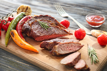 Board with tasty cut grilled meat on wooden table