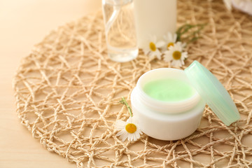 Jar of cream and chamomile flowers on table