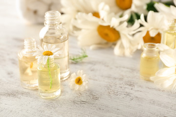 Bottles of essential oil with chamomile flowers on wooden table