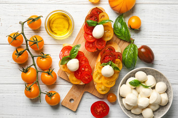 Fresh cherry tomatoes, mozzarella cheese and tasty sandwiches on wooden table, top view