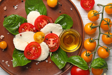 Fresh sliced cherry tomatoes, mozzarella cheese and bowl with olive oil on plate, top view