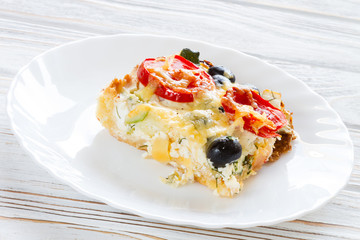 Vegetarian salt pie, Quiche with tomatoes, olives and feta cheese on white plate.
