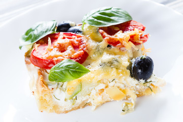 Vegetarian salt pie, Quiche with tomatoes, olives and feta cheese on white plate.