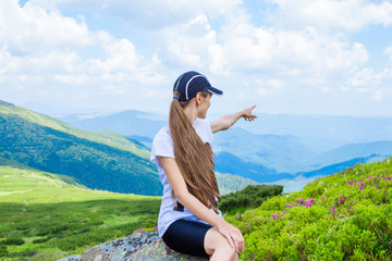 Hiking girl at peak of mountain points to something. Enjoy the mountain view