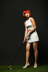 attractive young woman in sportswear and high heels playing golf on green grass on grey