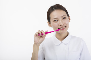 歯ブラシを持って微笑む白衣とピンクのエプロンを着た女性