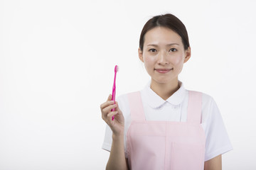 歯ブラシを持って微笑む白衣とピンクのエプロンを着た女性