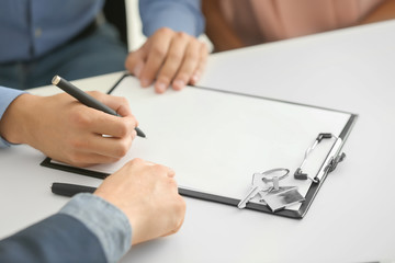 Young man signing a contract for buying house in office of estate agent