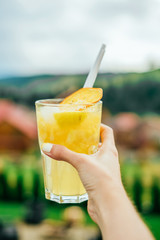 Citrus lemonade in the hand of young woman with the mountain view.