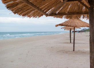 Fototapeta na wymiar several straw umbrellas on the beach in autumn. End of the turistic season. No one around. Empty beach.