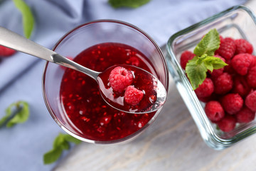 Glass and bowls with tasty raspberry jam on wooden table
