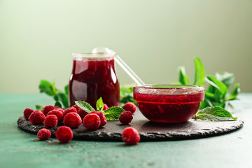 Slate plate with glass jar and bowl of tasty raspberry jam on green table