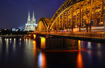 Fototapeta premium Night panorama of Cologne, Germany, with the river Rhine, the railway Hohenzollern Bridge and Cologne Cathedral, a famous landmark and a largest gothic church in Northern Europe